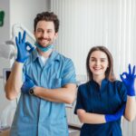 photo-smiling-dentist-standing-with-arms-crossed-with-her-colleague-showing-okay-sign-min